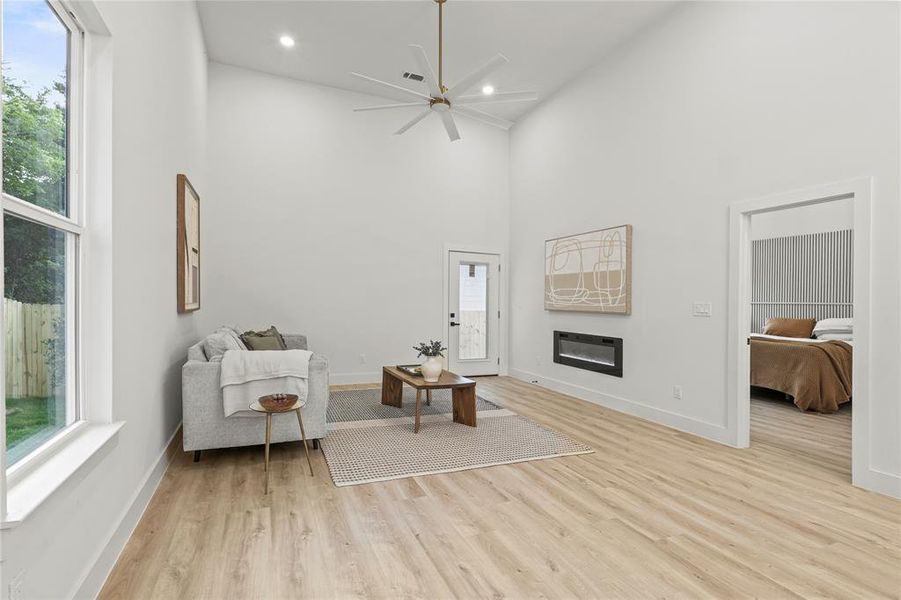 Living area featuring high vaulted ceiling, light wood-style flooring, a ceiling fan, a glass covered fireplace, and baseboards Living area featuring high vaulted ceiling, light wood-style flooring, a ceiling fan, a glass covered fireplace, and baseboards