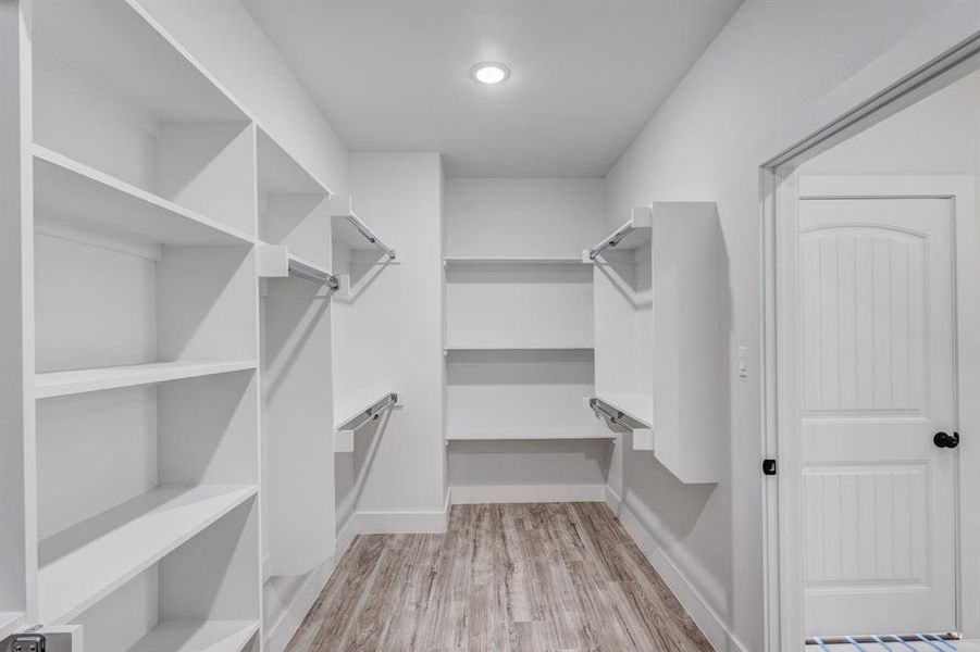 Walk in closet with light hardwood / wood-style floors