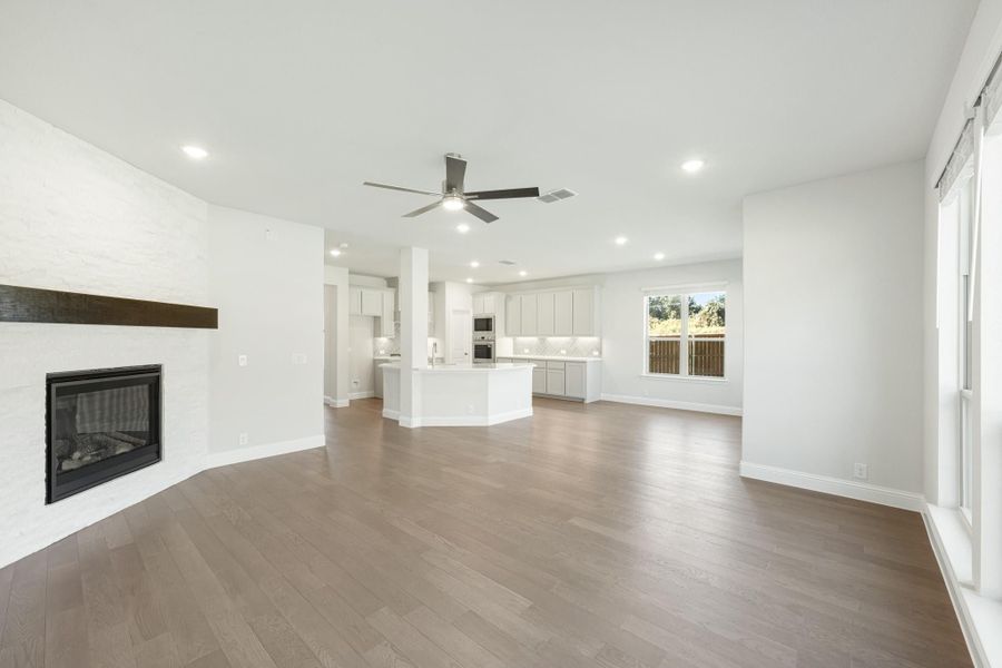 Open-concept living room with stone fireplace, hardwood floors, and kitchen island visible in background