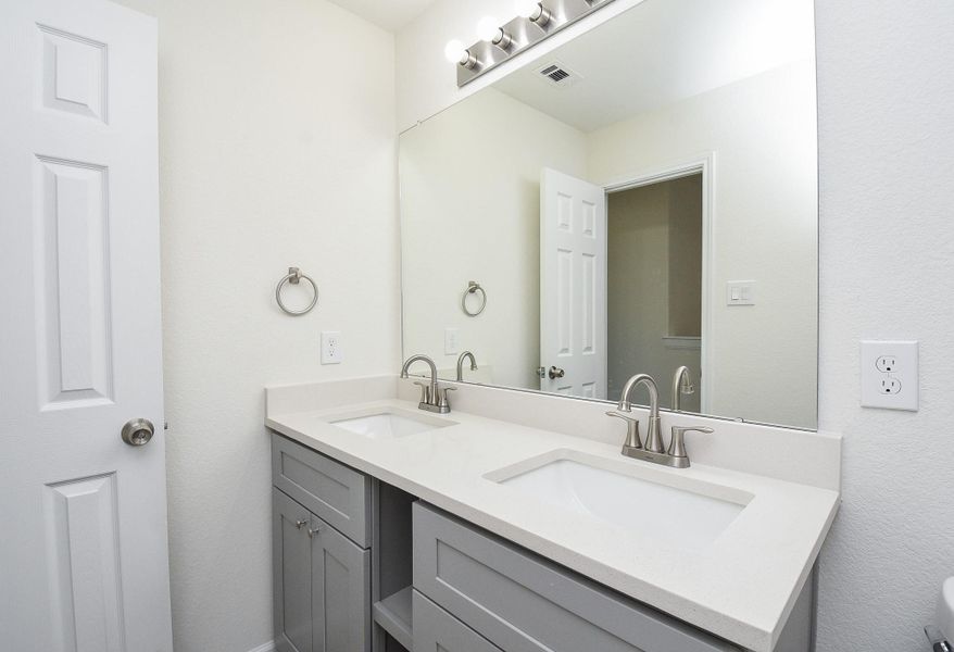 This is a clean and modern bathroom featuring a double sink vanity with a large mirror and ample lighting, set against a neutral color palette. This is a clean and modern bathroom featuring a double sink vanity with a large mirror and ample lighting, set against a neutral color palette.