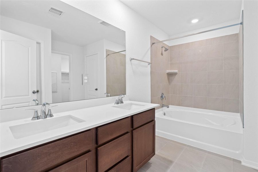 This beautiful move-in ready primary bathroom showcases a tub/shower combination with tile surround, stained cabinetry paired with light countertops, dual vanity sinks, a large mirror, a spacious walk-in closet with built-in shelving, high ceilings, custom paint, and stylish modern finishes throughout. This beautiful move-in ready primary bathroom showcases a tub/shower combination with tile surround, stained cabinetry paired with light countertops, dual vanity sinks, a large mirror, a spacious walk-in closet with built-in shelving, high ceilings, custom paint, and stylish modern finishes throughout.