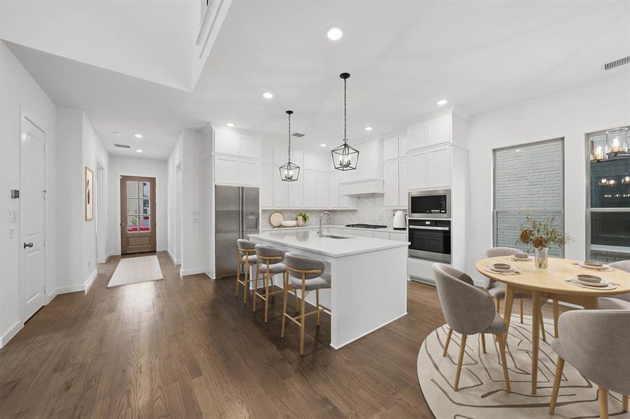 Kitchen with white cabinetry, a kitchen island with sink, a kitchen breakfast bar, appliances with stainless steel finishes, and dark wood finished floors