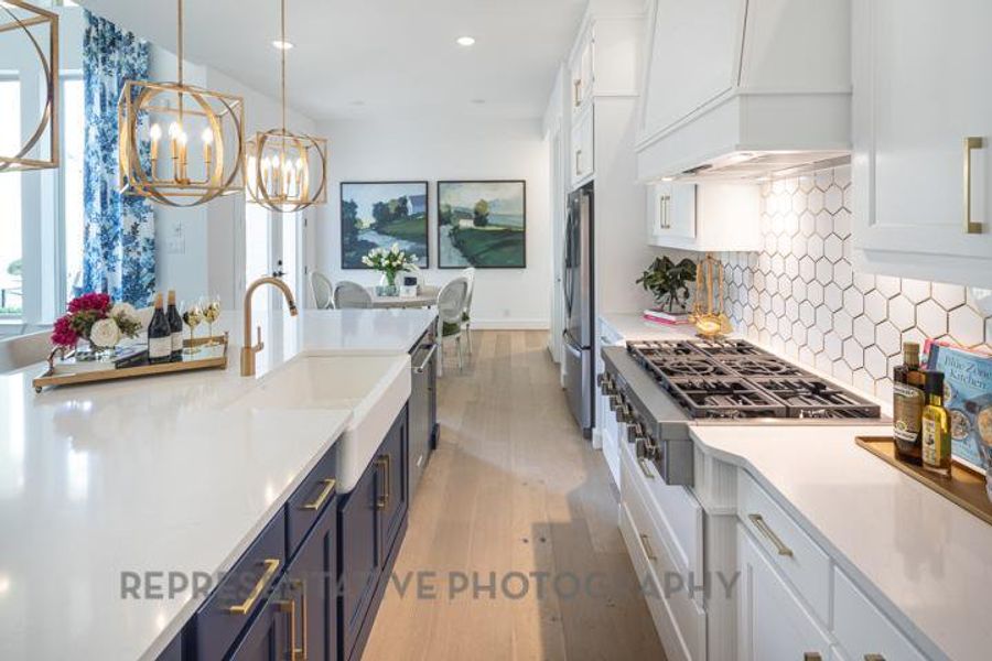 Kitchen featuring custom exhaust hood, light wood-style flooring, white cabinetry, a notable chandelier, and appliances with stainless steel finishes Kitchen featuring custom exhaust hood, light wood-style flooring, white cabinetry, a notable chandelier, and appliances with stainless steel finishes