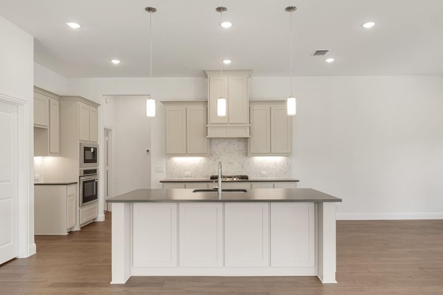 Kitchen with large center island, gray countertops, cream cabinets, pendant lights, and hardwood floors