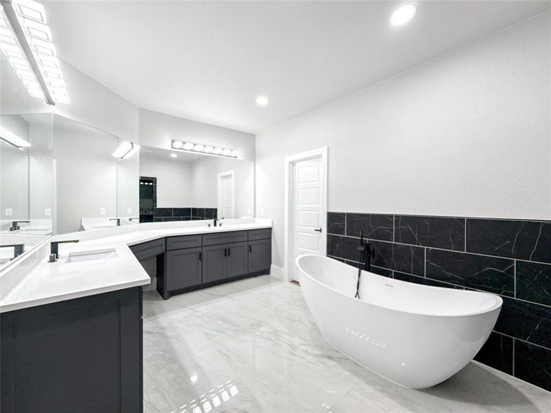 Bathroom featuring a freestanding tub, two vanities, recessed lighting, tile walls, and light marble finish floors