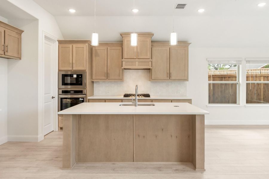 Kitchen with large center island, light wood cabinets, stainless steel appliances, and pendant lights overhead.
