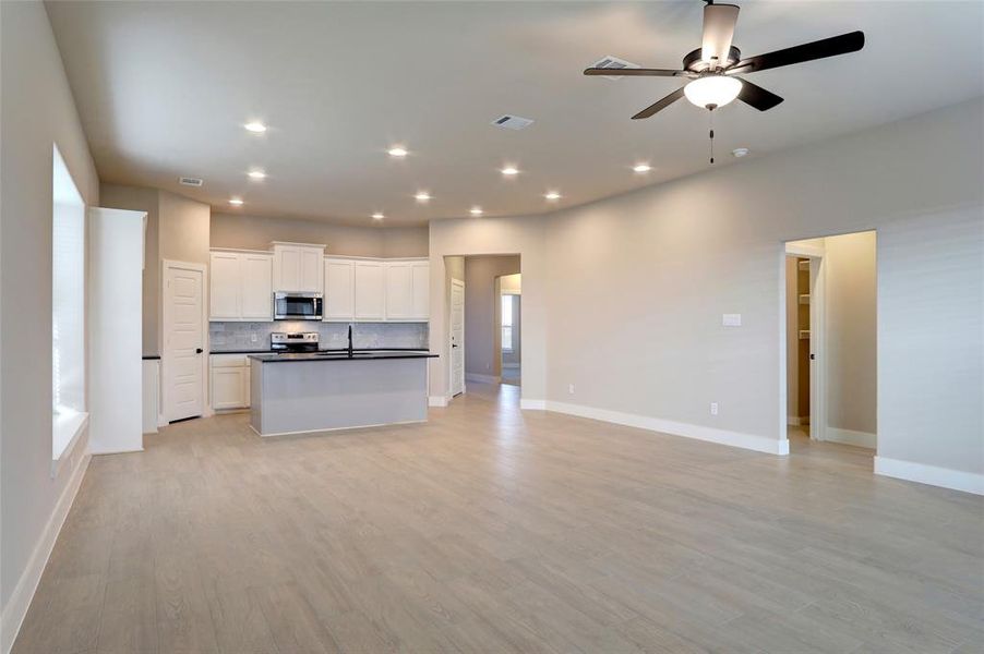 Kitchen featuring light hardwood / wood-style floors, white cabinets, stainless steel appliances, a kitchen island with sink, and backsplash