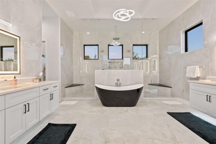 The serene primary suite is a private retreat complete with a spa-inspired bath featuring a soaking tub, oversized walk-in shower, custom-designed closet, and tranquil wooded vistas.