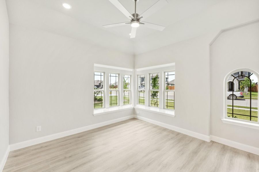 Empty room with light wood floors, ceiling fan, and corner bay windows overlooking a neighborhood Empty room with light wood floors, ceiling fan, and corner bay windows overlooking a neighborhood