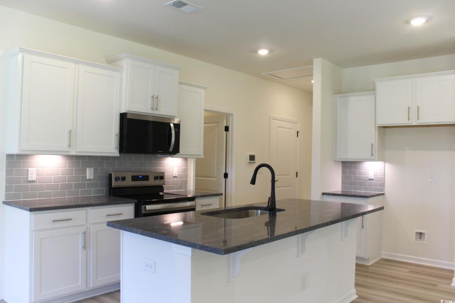 Kitchen featuring tasteful backsplash, stainless steel appliances, white cabinetry, dark stone countertops, and recessed lighting Kitchen featuring tasteful backsplash, stainless steel appliances, white cabinetry, dark stone countertops, and recessed lighting