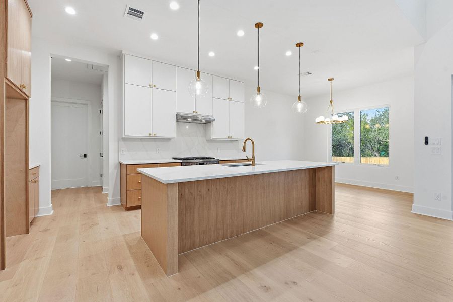 An expansive kitchen layout showcases light hardwood flooring, custom cabinetry, and a large central island.