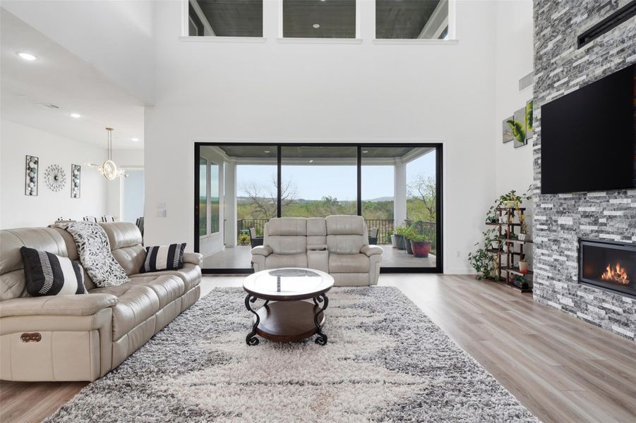 Expansive living area featuring high ceilings, a contemporary fireplace with a stacked stone facade, and large sliding glass doors leading to an outdoor patio with scenic views