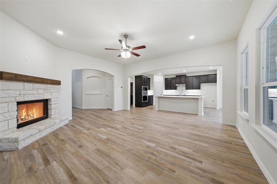 Unfurnished living room featuring ceiling fan, a stone fireplace, arched walkways, light wood finished floors, and recessed lighting