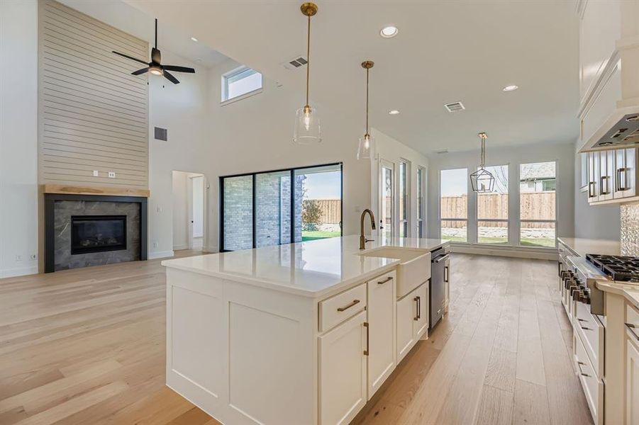 Kitchen featuring white cabinets, open floor plan, light wood finished floors, a tile fireplace, and a kitchen island with sink