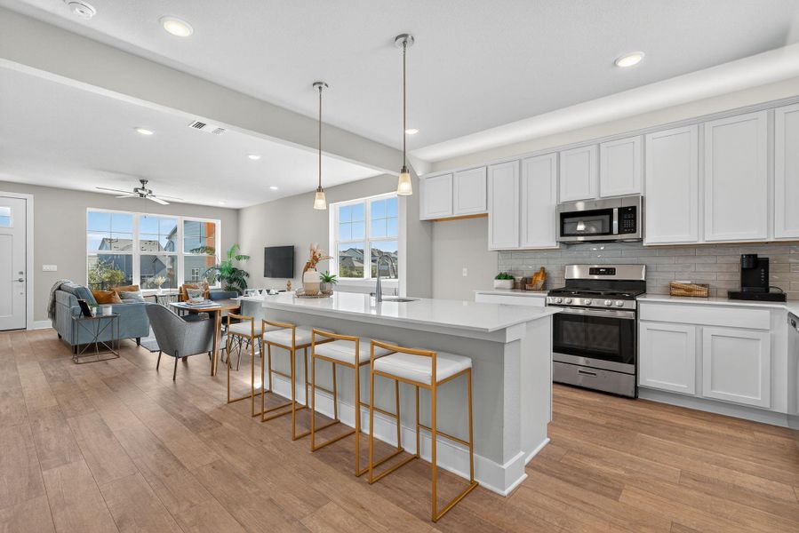 Kitchen with appliances with stainless steel finishes, hanging light fixtures, a kitchen island with sink, white cabinetry, and tasteful backsplash