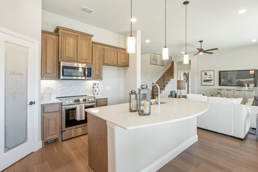 Kitchen with curved island, wood cabinets, stainless appliances, and open view to living room with hardwood floors