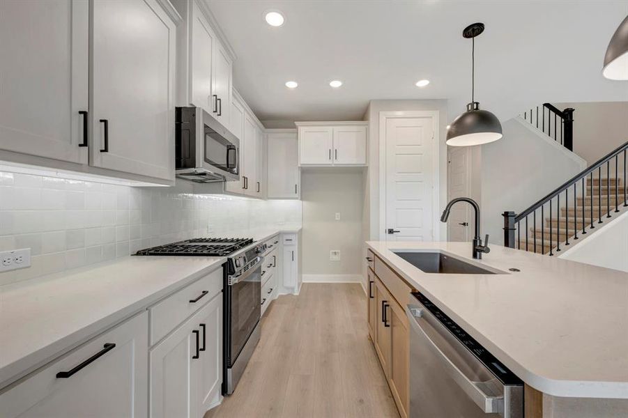 Kitchen featuring two tone cabinets, stainless steel appliances, light wood finished floors, a center island with sink, and decorative light fixtures