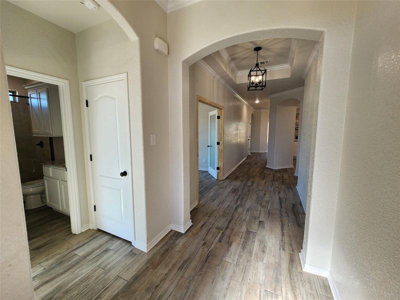 Hall with crown molding, arched walkways, a raised ceiling, light wood-style floors, and a textured wall