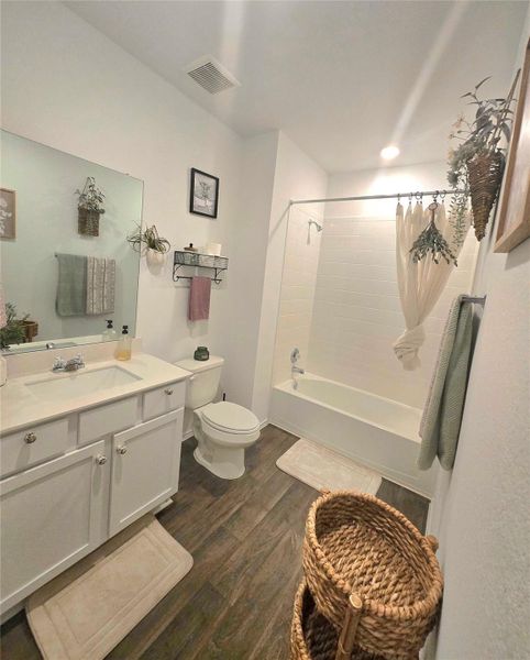 Bathroom featuring a single vanity with storage, wood-finish flooring, a toilet, and a bathtub with a shower