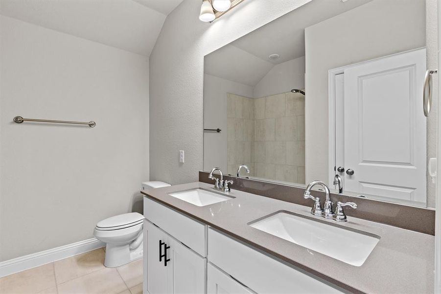 Bathroom featuring toilet, tile patterned floors, vanity, a tile shower, and vaulted ceiling