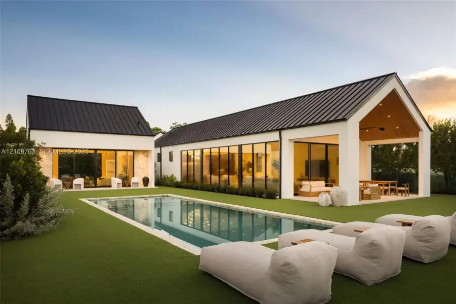 Contemporary residence featuring a white stucco exterior, metal roofing, expansive glass wall panels, an integrated covered patio, and a rectangular in-ground swimming pool