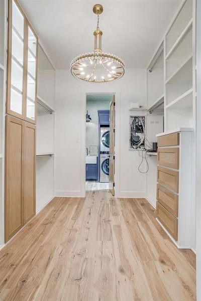 Walk in closet featuring stacked washer / dryer, a chandelier, and light wood-style floors