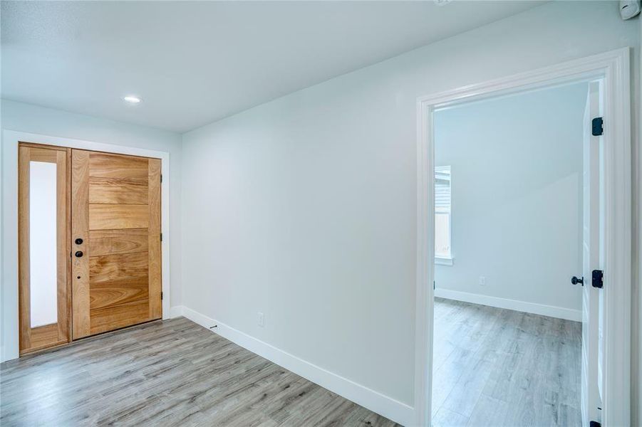 Entryway featuring a solid wood-finish door with sidelight, overhead recessed lighting, light wood-finish flooring, and crisp white baseboards