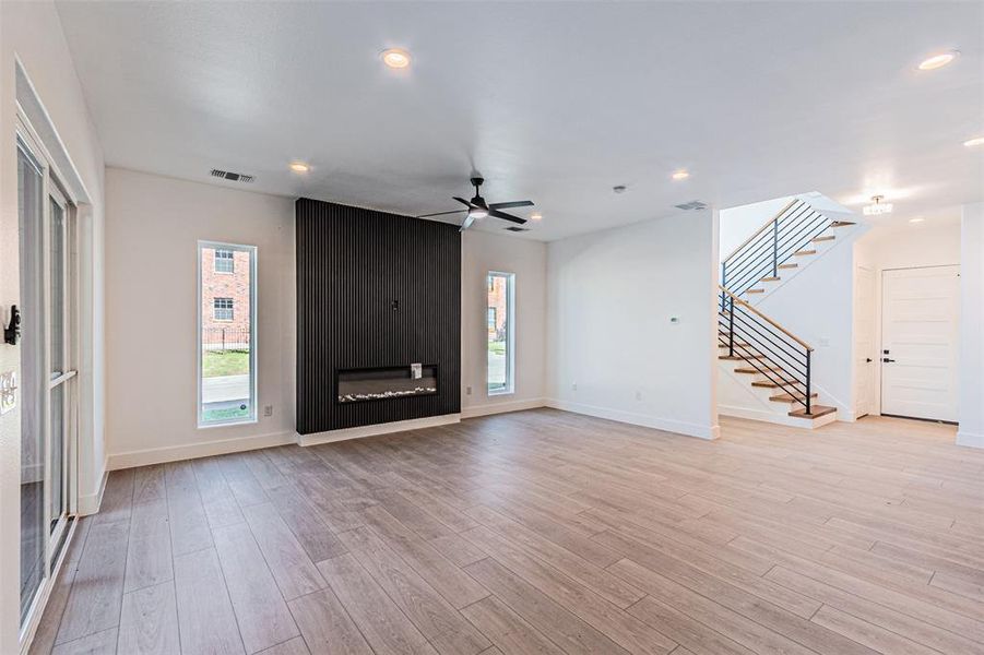 Unfurnished living room with stairway, light wood-type flooring, recessed lighting, a ceiling fan, and a large fireplace