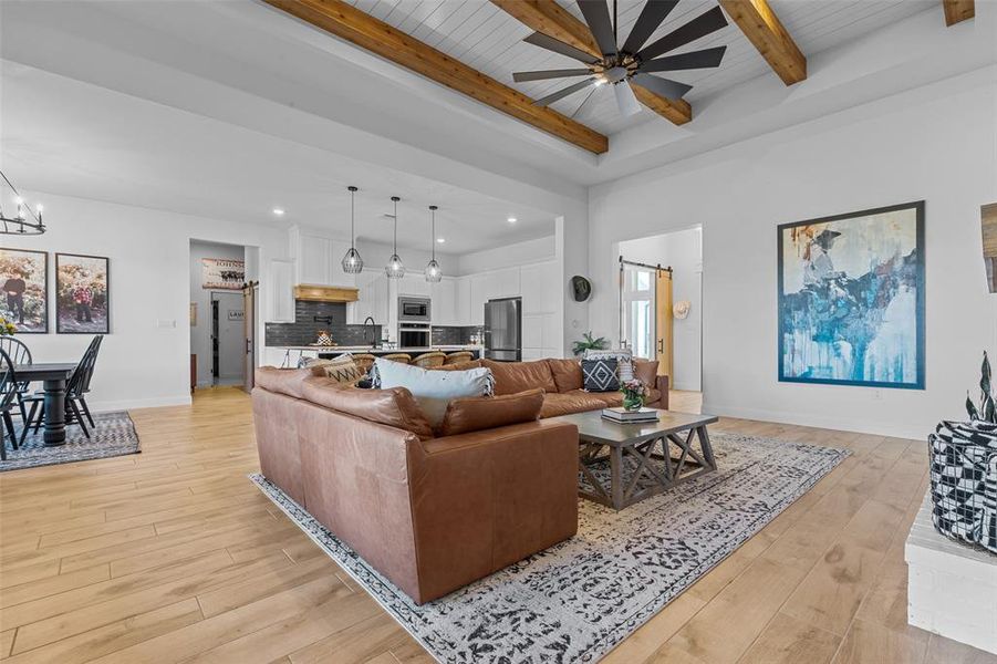 Living room with ceiling fan with notable chandelier, sink, a barn door, light wood-type flooring, and beam ceiling