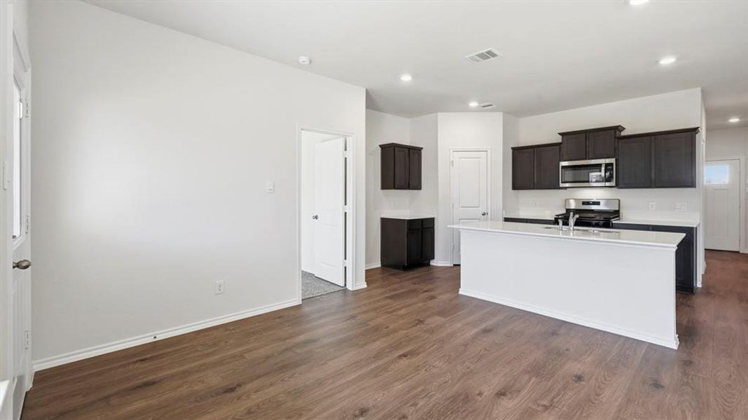 Kitchen with appliances with stainless steel finishes, a kitchen island with sink, dark wood-type flooring, recessed lighting, and light stone countertops Kitchen with appliances with stainless steel finishes, a kitchen island with sink, dark wood-type flooring, recessed lighting, and light stone countertops