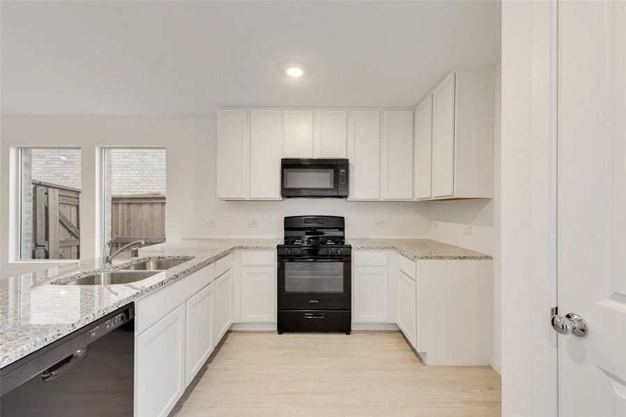 Kitchen with black appliances, sink, white cabinets, light hardwood / wood-style floors, and light stone counters