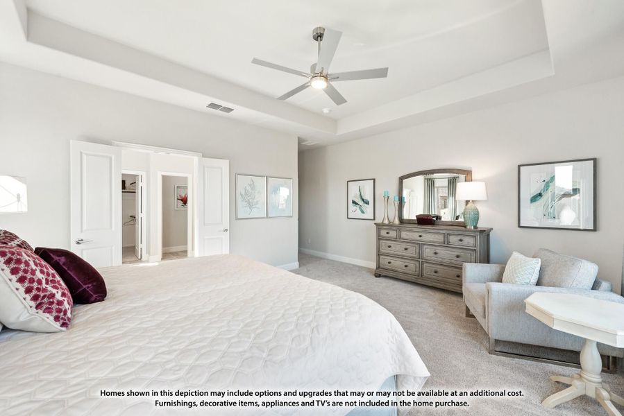 Master bedroom with tray ceiling, ceiling fan, carpet flooring, and doors leading to walk-in closet and bathroom