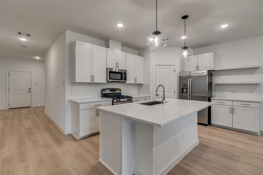 Kitchen with tasteful backsplash, decorative light fixtures, open shelves, appliances with stainless steel finishes, and recessed lighting Kitchen with tasteful backsplash, decorative light fixtures, open shelves, appliances with stainless steel finishes, and recessed lighting