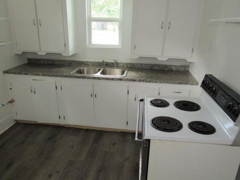 Kitchen with white electric range oven, white cabinets, dark wood-style flooring, and dark countertops Kitchen with white electric range oven, white cabinets, dark wood-style flooring, and dark countertops