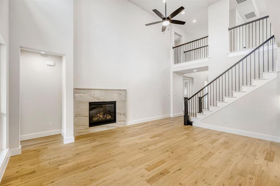 Two-story living area featuring a fireplace with a stone surround, light wood-finish flooring, and a ceiling fan