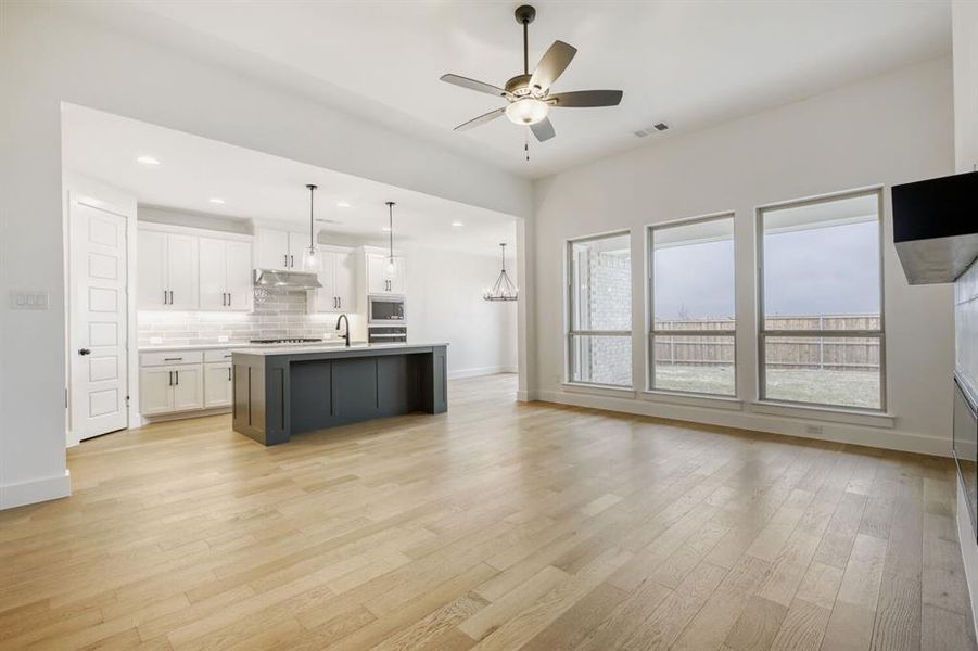 Two tone kitchen with open floor plan, dual tone cabinets, a ceiling fan, light countertops, and a kitchen island with sink