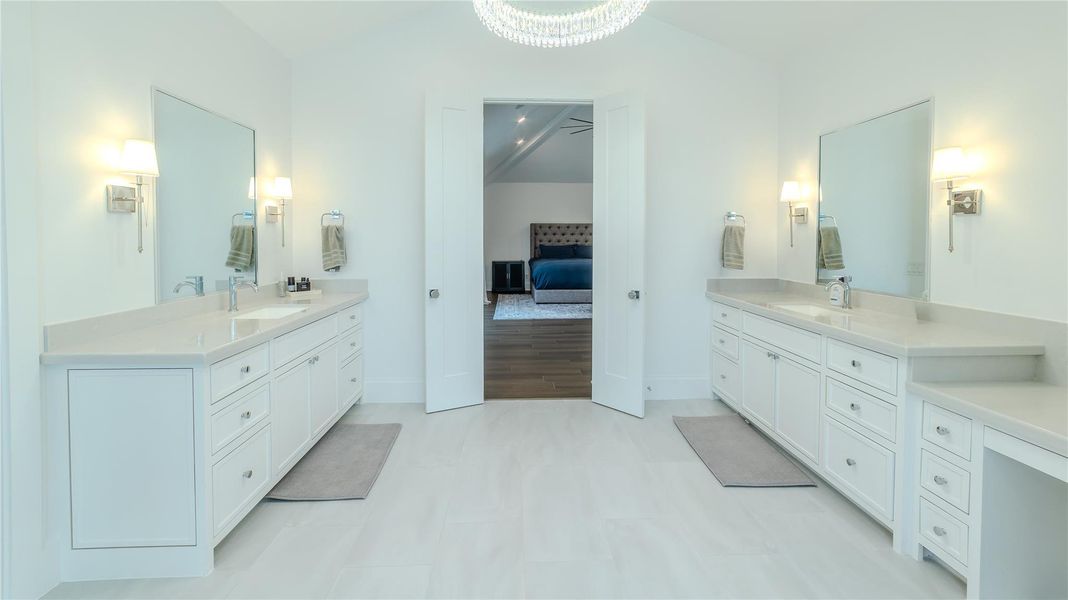 This spacious bathroom features dual vanities with ample storage, elegant lighting, and a pristine white finish. The room connects seamlessly to a bedroom, offering convenience and style.