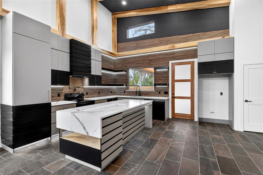 Kitchen featuring modern cabinets, light stone counters, a kitchen island, dual tone cabinetry, and a high ceiling Kitchen featuring modern cabinets, light stone counters, a kitchen island, dual tone cabinetry, and a high ceiling