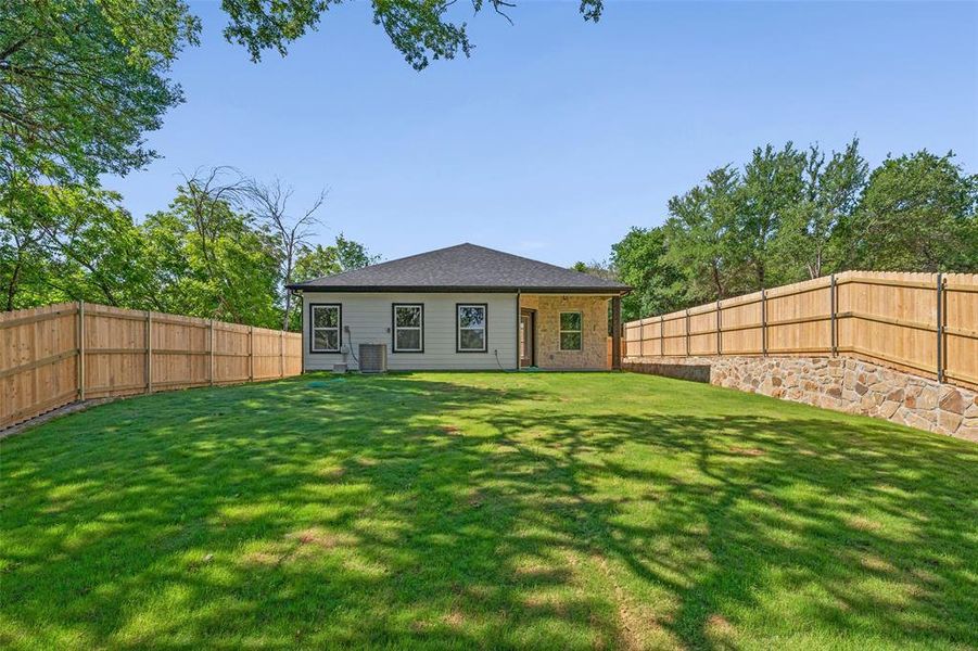 Spacious backyard featuring a manicured lawn, full privacy fencing, and a stone retaining wall