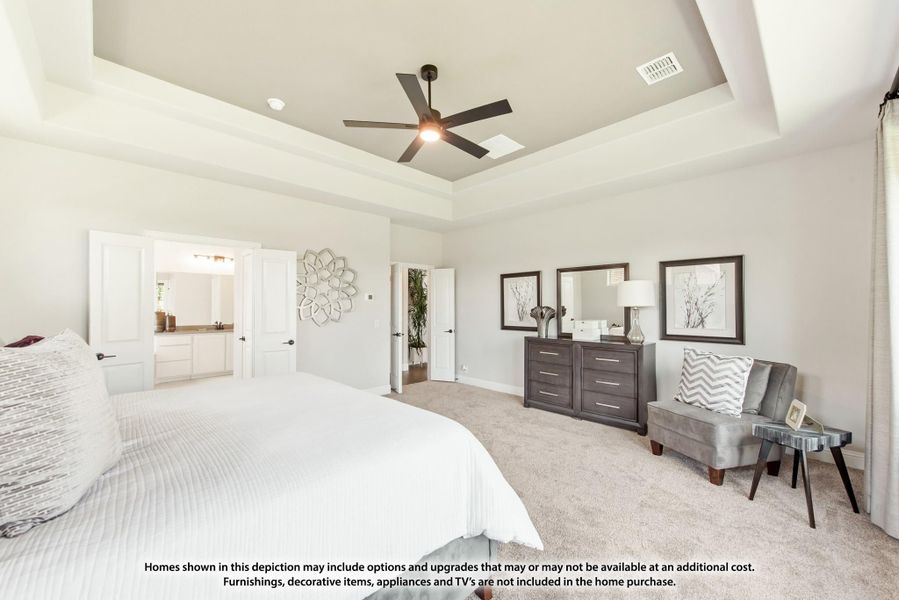 Master bedroom with tray ceiling, ceiling fan, carpet floors, and ensuite bathroom access