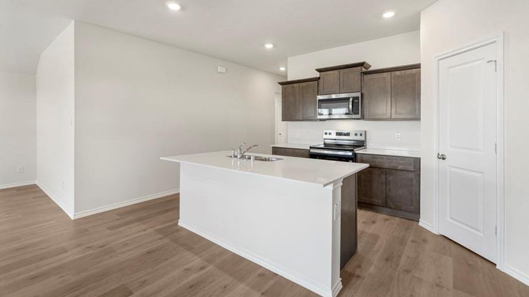 Kitchen featuring a central island with an undermount sink, wood-finish flooring, recessed lighting, stainless steel appliances, and shaker-style cabinetry