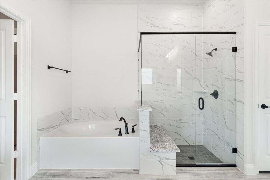 Master bathroom with soaking tub, glass walk-in shower, and white marble tile walls with black fixtures