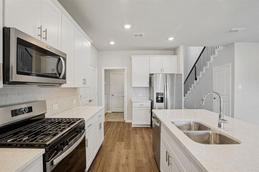 Kitchen featuring stainless steel appliances, white cabinetry, light stone counters, light wood-type flooring, and recessed lighting