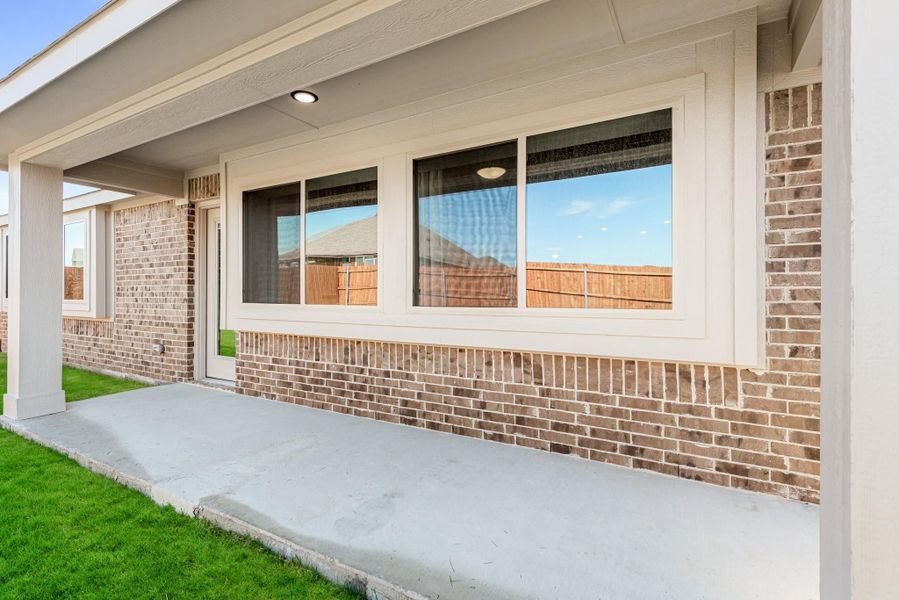 Covered back patio with concrete slab, brick exterior wall, large windows, and green lawn Covered back patio with concrete slab, brick exterior wall, large windows, and green lawn