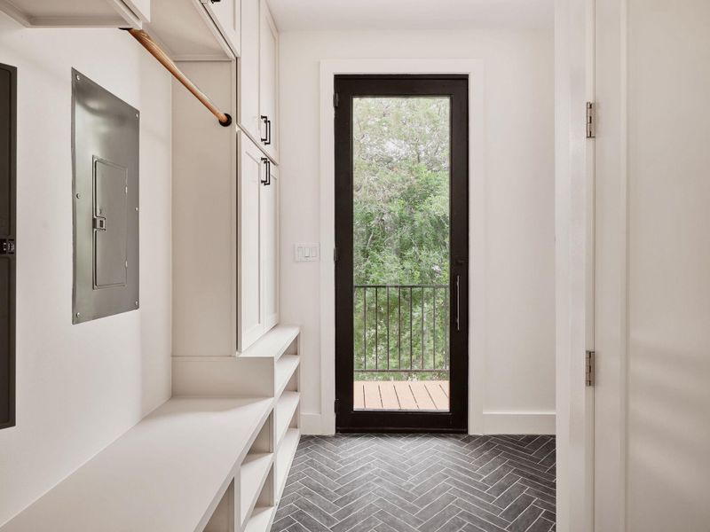 Mudroom entry featuring herringbone-patterned floor tiles, built-in white cabinetry, a built-in bench with integrated shelving, a clothes rod, and a full-light exterior door leading to a balcony with metal railing
