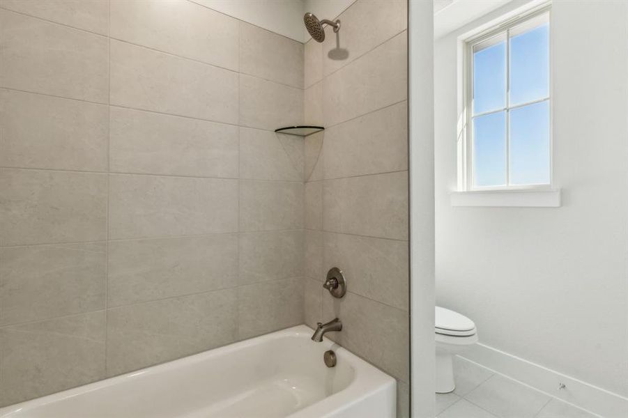 Bathroom featuring tiled shower / bath, tile patterned floors, and toilet