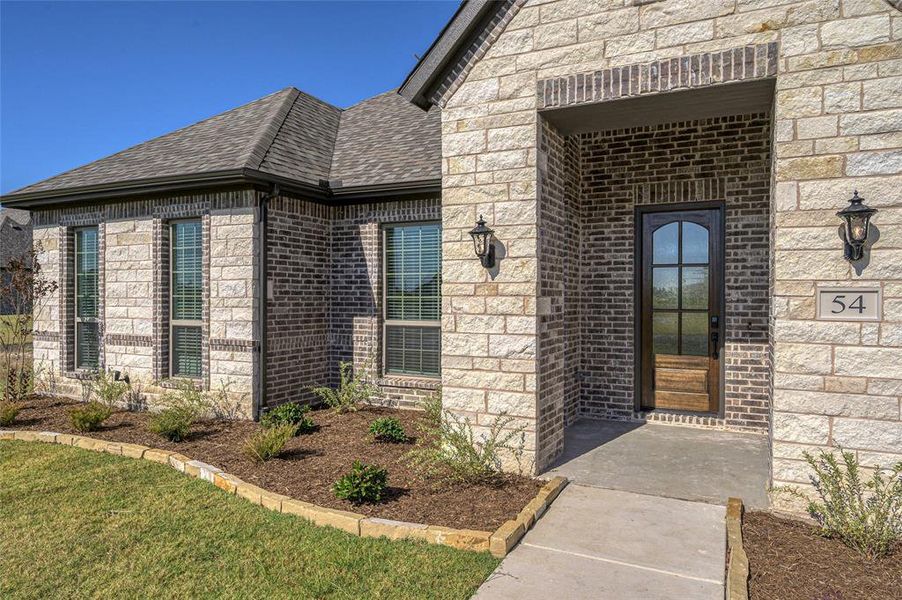 Property entrance with roof with shingles, brick siding, and a lawn