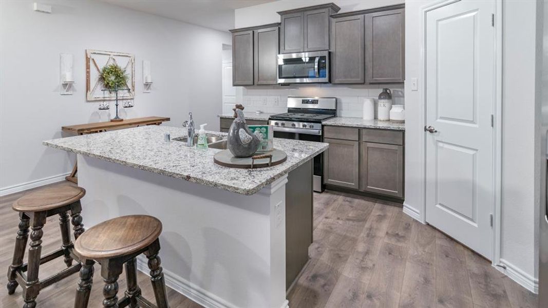 Kitchen with appliances with stainless steel finishes, tasteful backsplash, a kitchen island with sink, light stone countertops, and a breakfast bar area Kitchen with appliances with stainless steel finishes, tasteful backsplash, a kitchen island with sink, light stone countertops, and a breakfast bar area