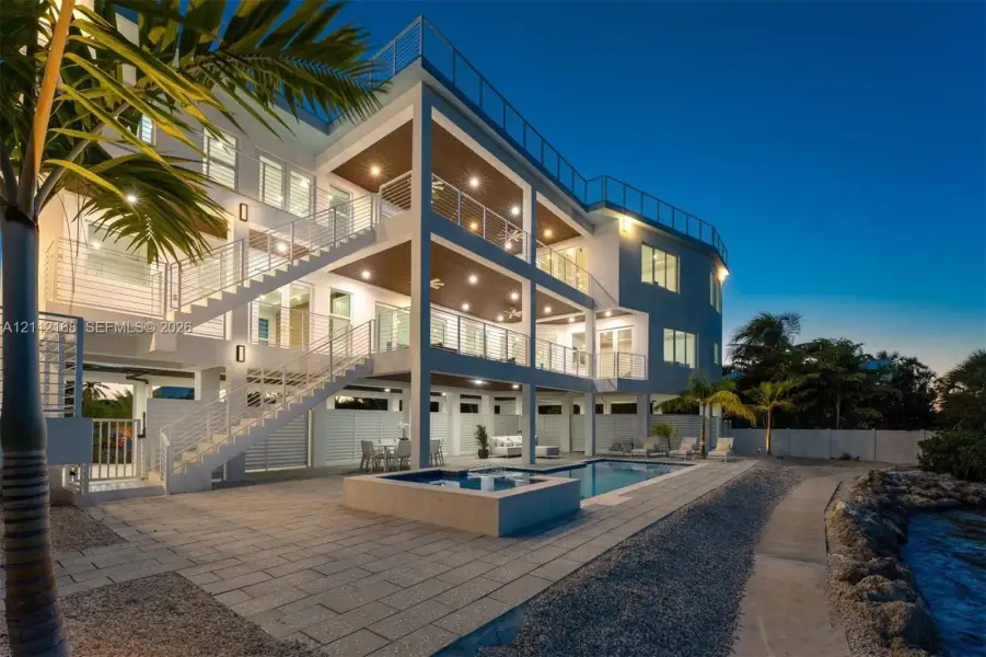 Multi-level exterior featuring stacked covered balconies, a rooftop terrace with horizontal cable railings, a built-in swimming pool and spa, and stone-paver hardscaping Multi-level exterior featuring stacked covered balconies, a rooftop terrace with horizontal cable railings, a built-in swimming pool and spa, and stone-paver hardscaping