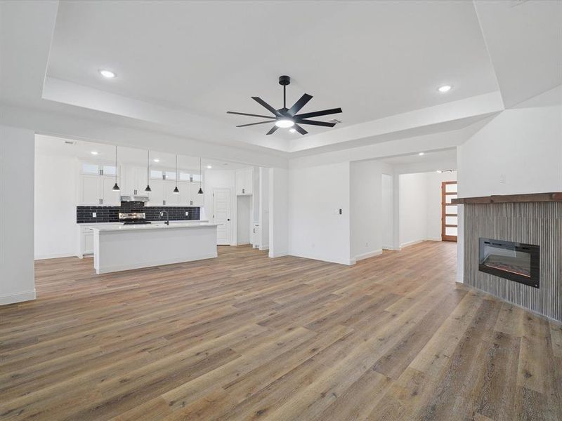Unfurnished living room with a glass covered fireplace, light wood-type flooring, a ceiling fan, a raised ceiling, and recessed lighting